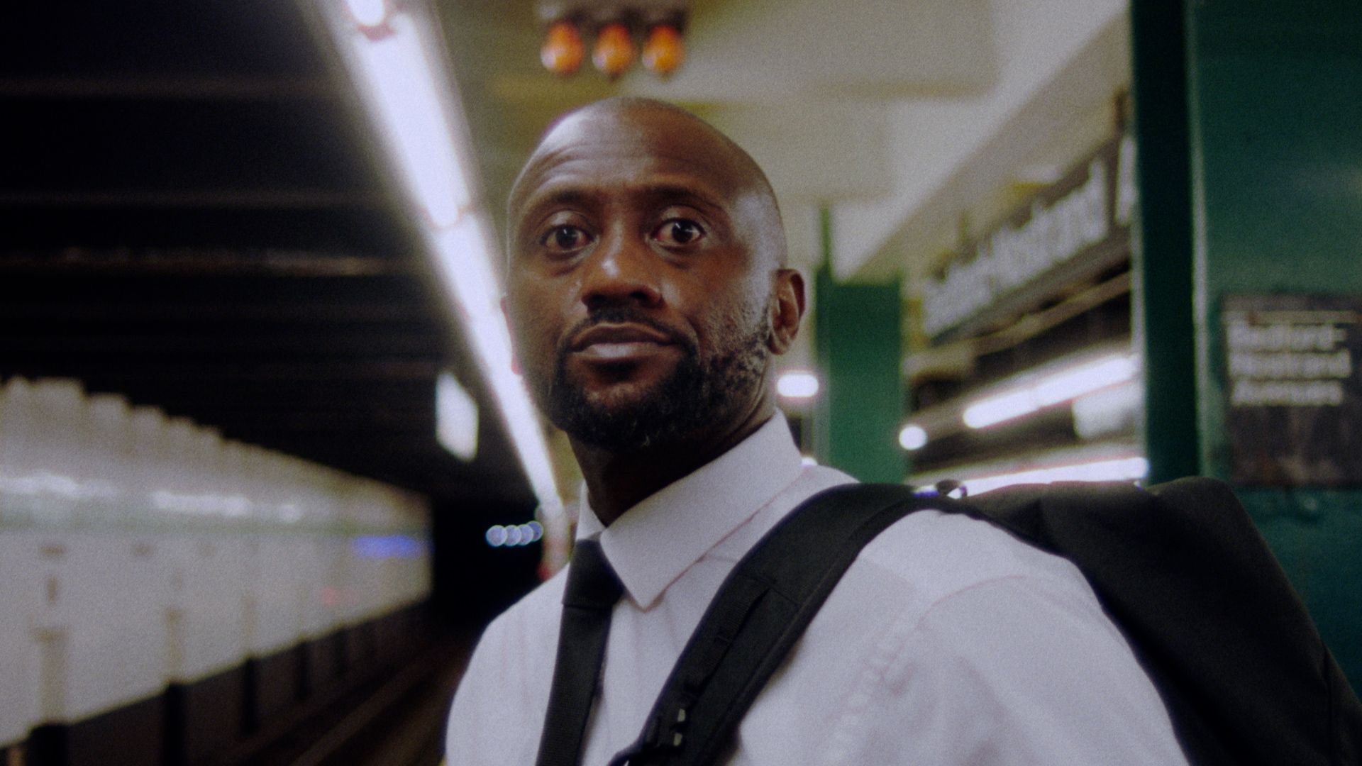 A man in a white shirt and tie on a subway platform.