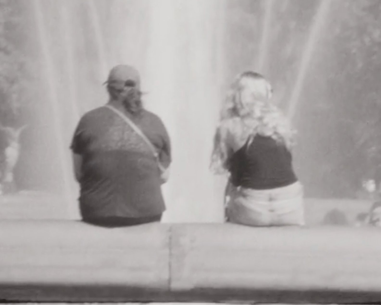 Two people sit on the edge of the Washington Square fountain, backs to the camera.